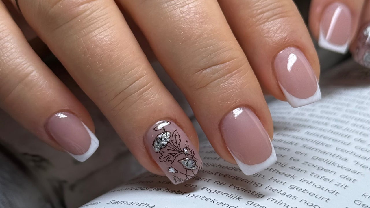 French manicure met een zwarte bloemtekening op één nagel, de hand rust op een open boek