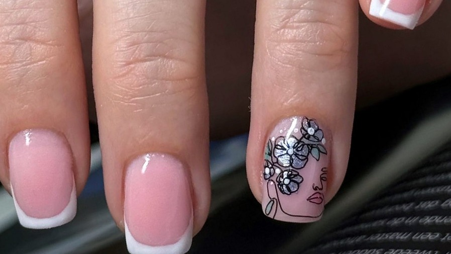 French nagels met een zwarte lijntekening van een bloem en een gezicht op één nagel